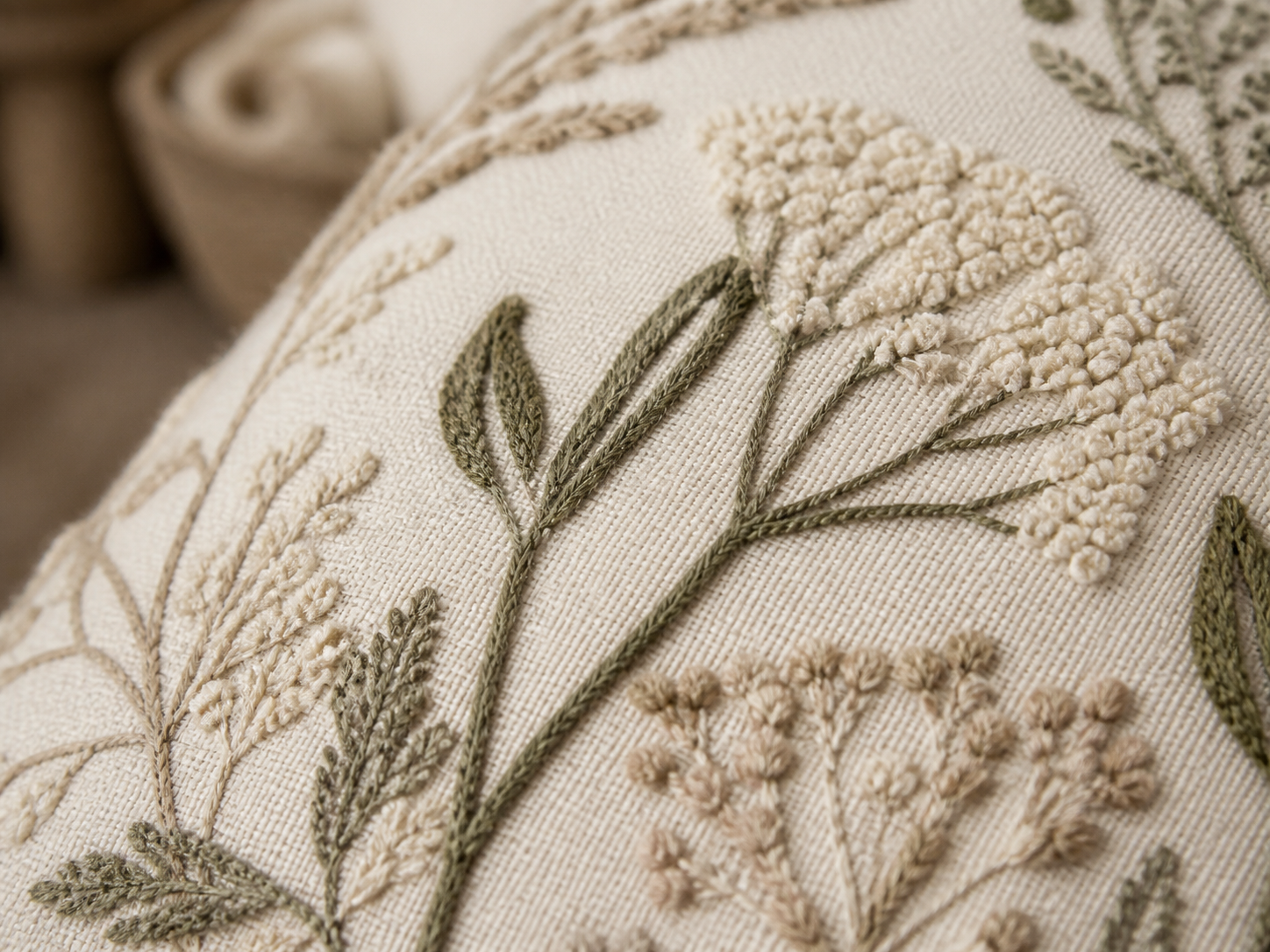 Close-up of botanical embroidery and raised tufting on ivory textile
